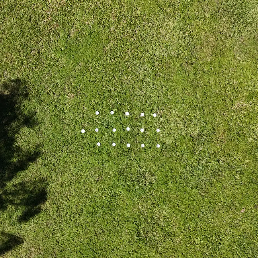 Sixteen white bowls laid out on grass beside a tree shadow, seen from a UAV at 15 m